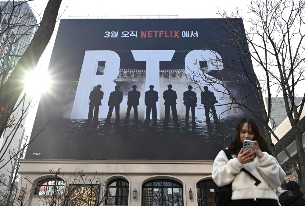 A woman uses her smartphone in front of a billboard promoting a comeback concert of K-pop boy group BTS at Gwanghwamun Square in Seoul on March 17, 2026. (Photo by Jung Yeon-je / AFP)
 