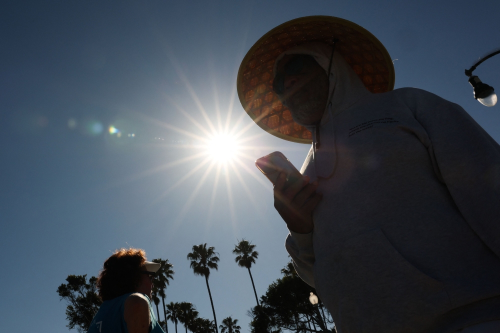A person wears a hat for shade under the morning sun while walking along The Strand in Redondo Beach, California on March 20, 2026, during a heat wave. (Photo by Patrick T. Fallon / AFP)