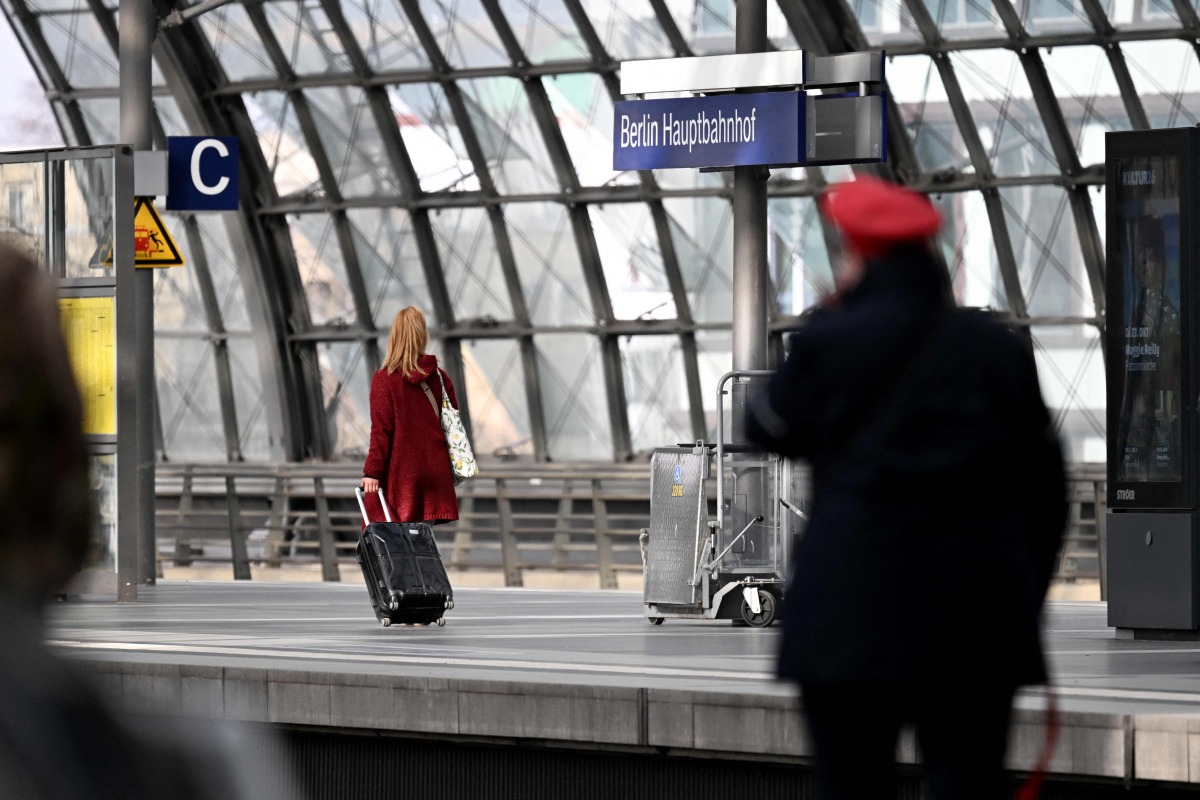 A traveller with suitcase and a train conductor walk along a platform at the main train station (Hauptbahnhof) in Berlin on March 27, 2026. Photo by RALF HIRSCHBERGER / AFP