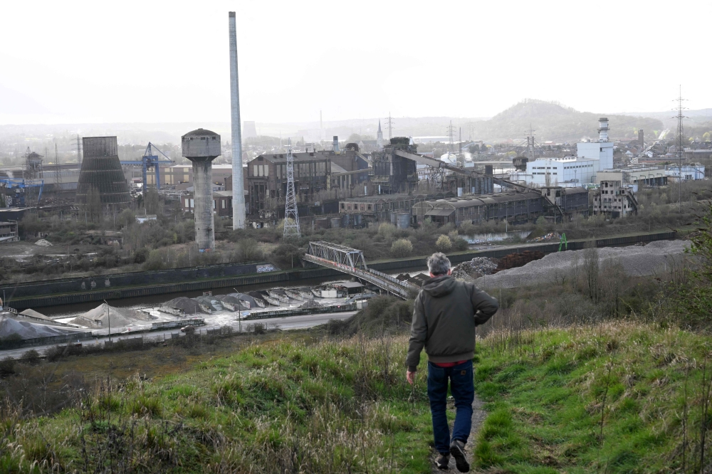 A tourist walks down a slag heap next to abandoned steel plants in Charleroi, southern Belgium, on March 11, 2026. (Photo by Nicolas Tucat / AFP)