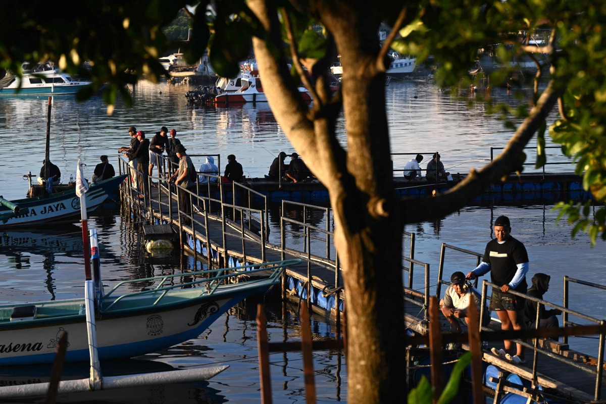 People fish at a pier near Denpasar on Indonesia's resort island of Bali on April 12, 2026. (Photo by SONNY TUMBELAKA / AFP)