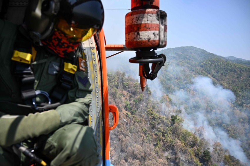 A Thai Department of Disaster Prevention and Mitigation (DDPM) personnel on a firefighting helicopter inspects fire spots to drop water to combat forest fires over Mae On district in the northern Thai province of Chiang Mai on March 26, 2025. Photo by MANAN VATSYAYANA / AFP