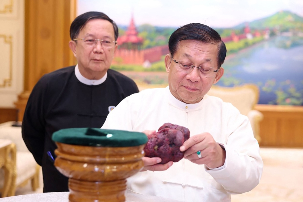 This handout photo taken and released on May 7, 2026 by Myanmar Radio and Television (MRTV) shows Myanmar president Min Aung Hlaing (R) holding an 11,000-carat ruby in Naypyidaw, after it was found at a gem tract in Mogok in Mandalay Region.  (Photo by Handout / Myanmar Radio and Television / AFP) /