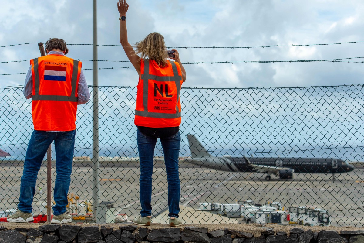 Representatives from the Netherlands embassy wave as a plane bound for the Netherlands carrying passengers evacuated from the Dutch-flagged hantavirus-stricken cruise ship MV Hondius prepares to take off from the Tenerife Sur-Reina Sofia airport on the island of Tenerife in Spain's Canary Islands on May 10, 2026. (Photo by Antonio Sempere / AFP)