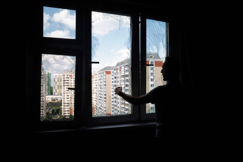 A local resident removes glass shards from a broken window in a residential building following an air attack in Krasnogorsk, Moscow region on May 17, 2026. (Photo by Tatyana Makeyeva / AFP)