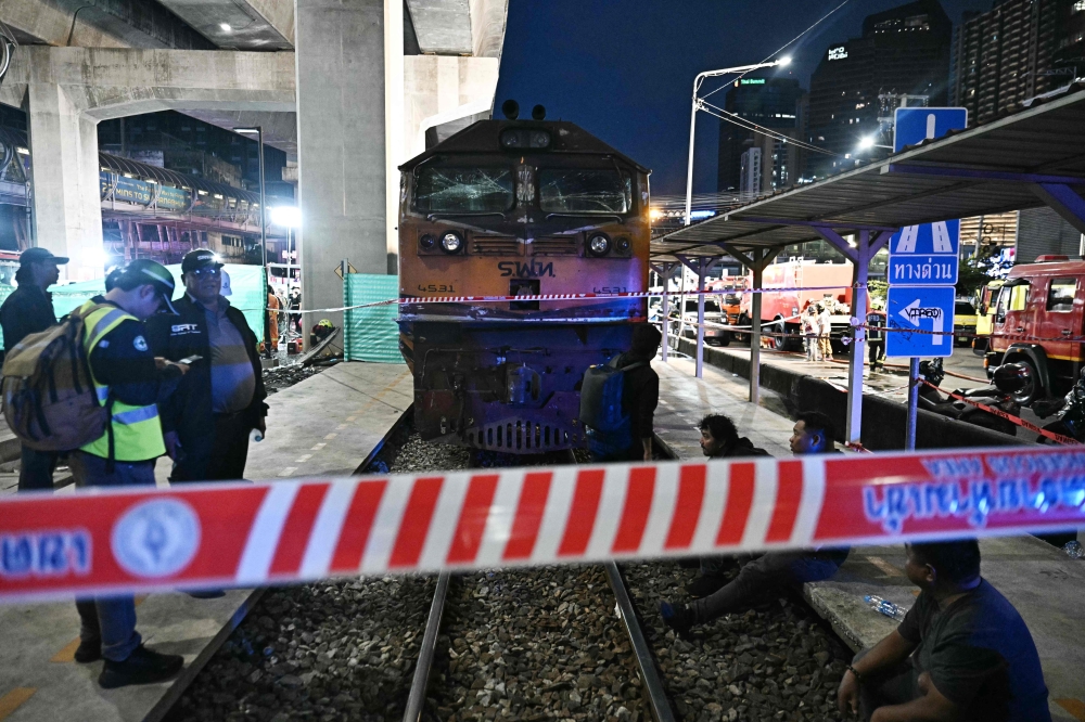 (Files) Officials stand next to the front of a train that collided with a bus underneath Makkasan Airport Rail station in Bangkok on May 16, 2026. (Photo by Lillian Suwanrumpha / AFP)
 
