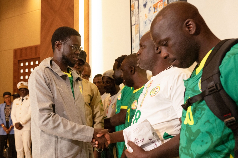 President of Senegal Bassirou Diomaye Faye (L) shakes hands with Senegalese supporters who were granted a royal pardon in Morocco as they arrive at Blaise Diagne International Airport in Ndiass, Senegal (Photo by Seyllou / AFP)