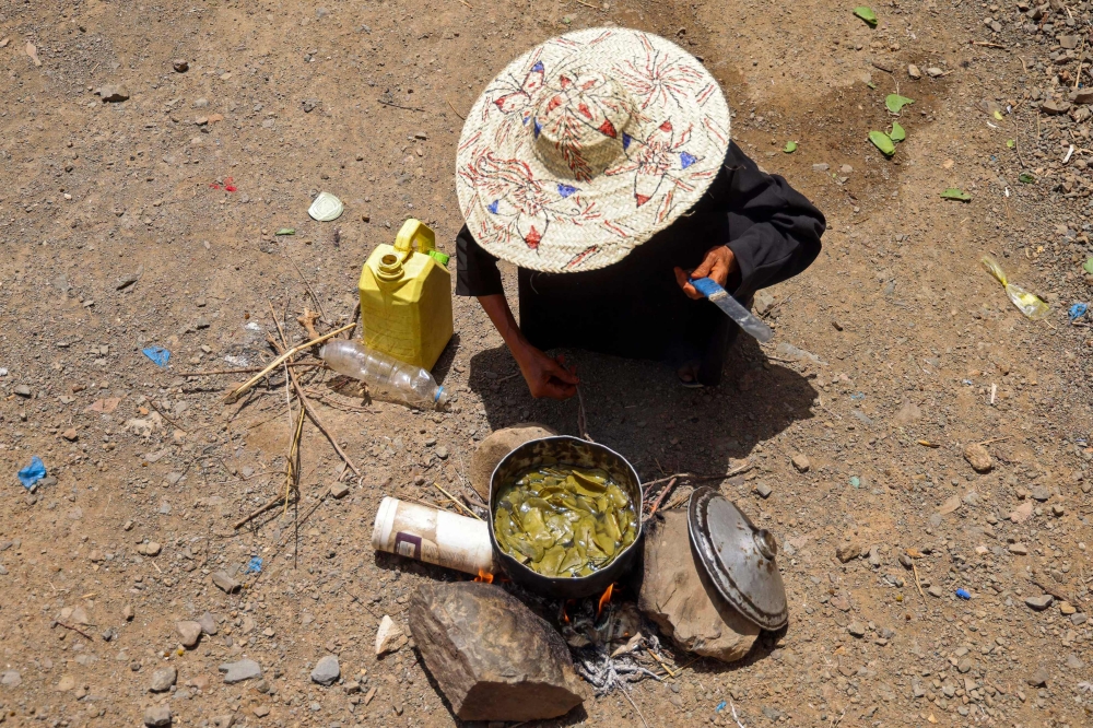 Displaced Yemeni woman Saeedah Mohammed boils tree leaves to feed her grand-children outside their makeshift tent in the Al-Manij displacement camp, near the city of Taez in Yemen's southwest, on May 21, 2026. (Photo by Ahmed al-Basha / AFP)