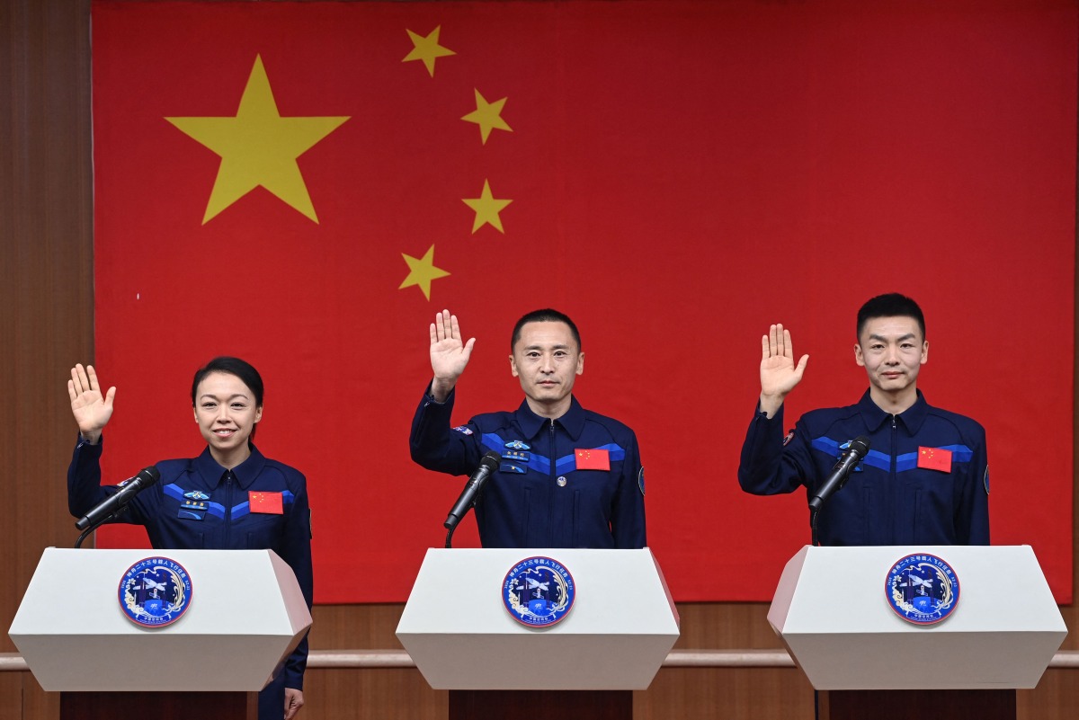 Astronauts for China's Shenzhou-23 space mission Lai Ka-ying (L), Zhu Yangzhu (C) and Zhang Zhiyuan (R) wave during a press conference before the launch of the mission at the Jiuquan Satellite Launch Center in the Gobi desert in Jiuquan, in northwestern China's Gansu province on May 23, 2026. (Photo by CNS / AFP)
