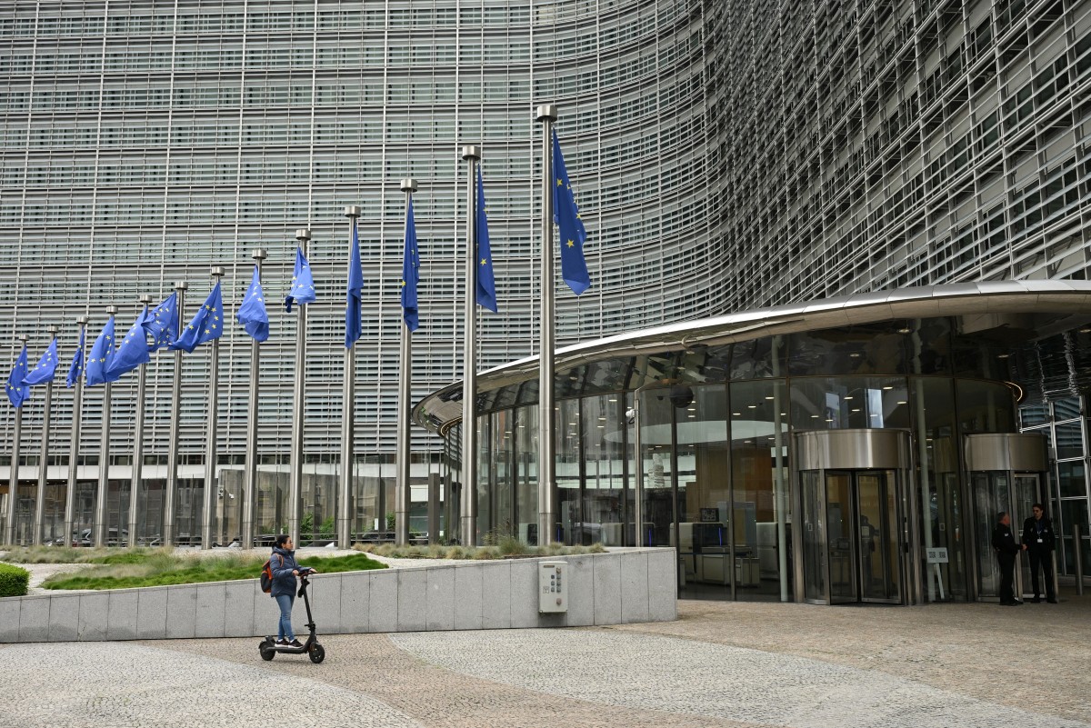 A woman rides an electric scooter past the Berlaymont building, the EU Commission headquarters, in Brussels on June 9, 2026. (Photo by Nicolas Tucat / AFP)
