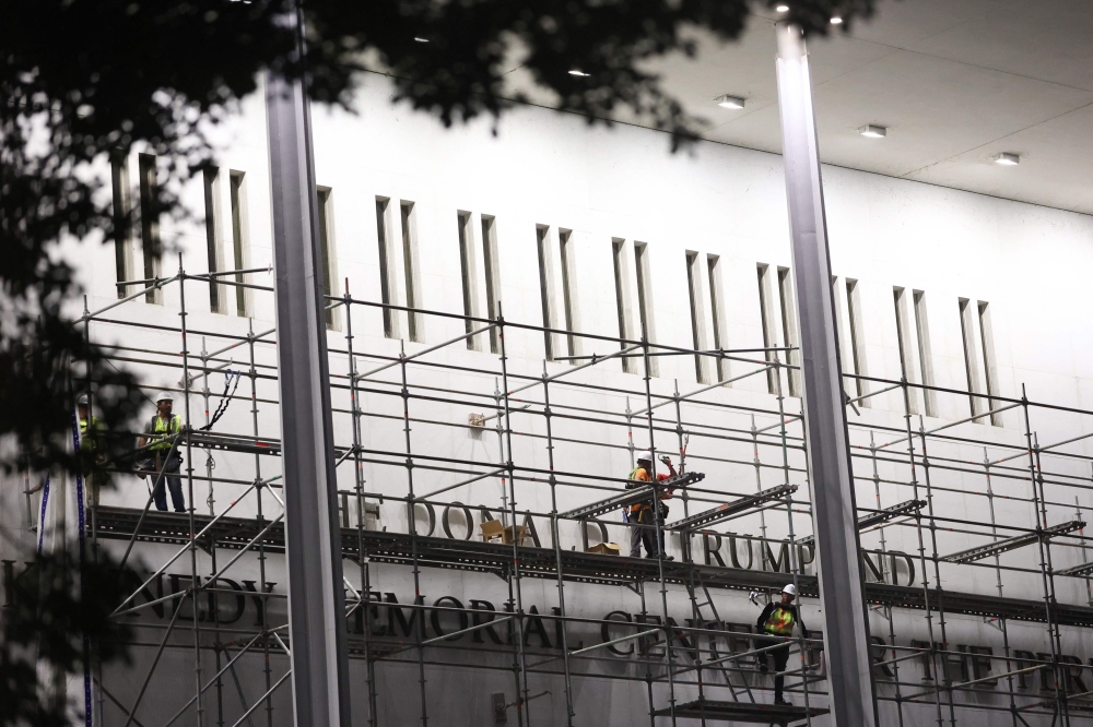 Workers build scaffolding near the signage for the 