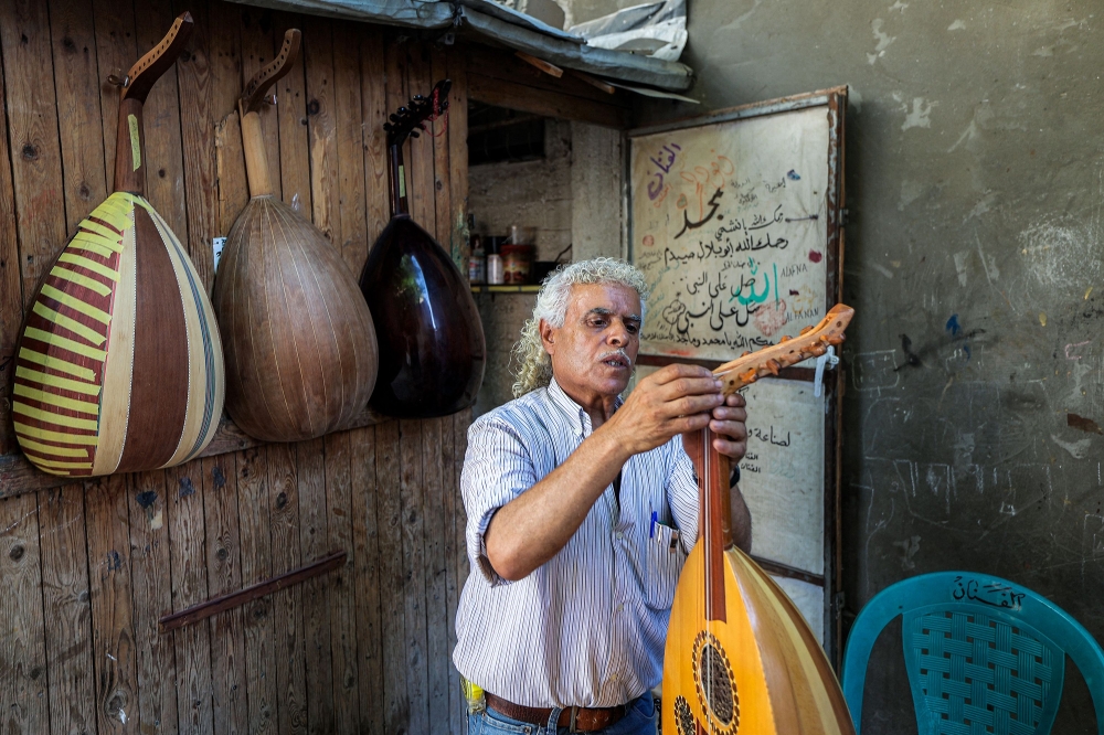 Displaced Palestinian craftsman Suhail Abu Shawish tunes a Oud musical instrument at his makeshift workshop in the Nuseirat camp for Palestinian refugees in the central Gaza Strip on June 23, 2026. (Photo by Eyad Baba / AFP)