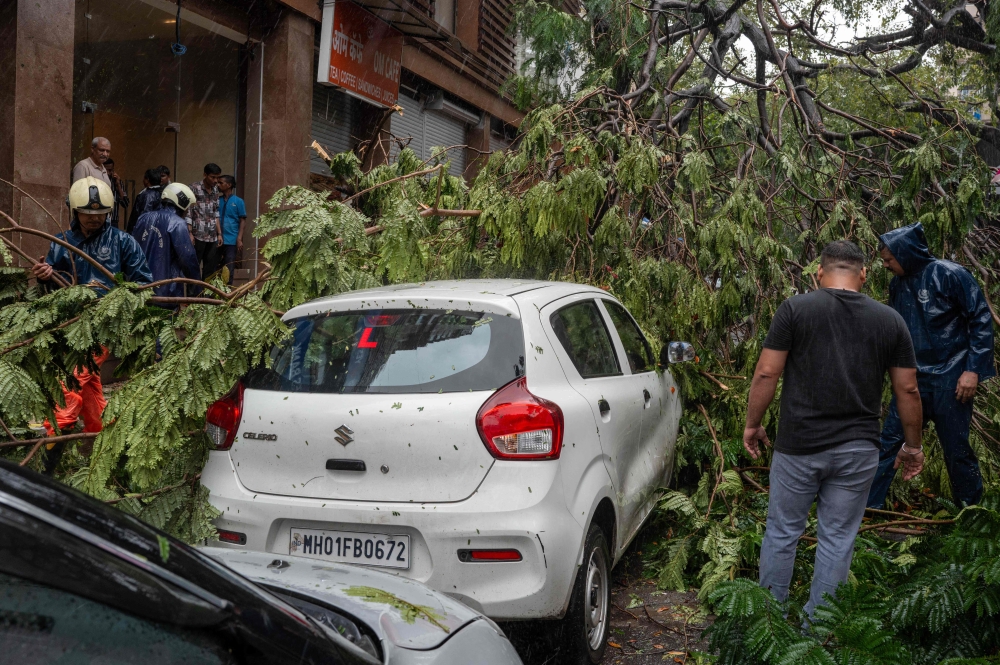 Civic-authority workers clear the road, blocked by uprooted trees following strong winds and heavy rainfall in Mumbai on July 5, 2026. (Photo by Punit Paranjpe / AFP