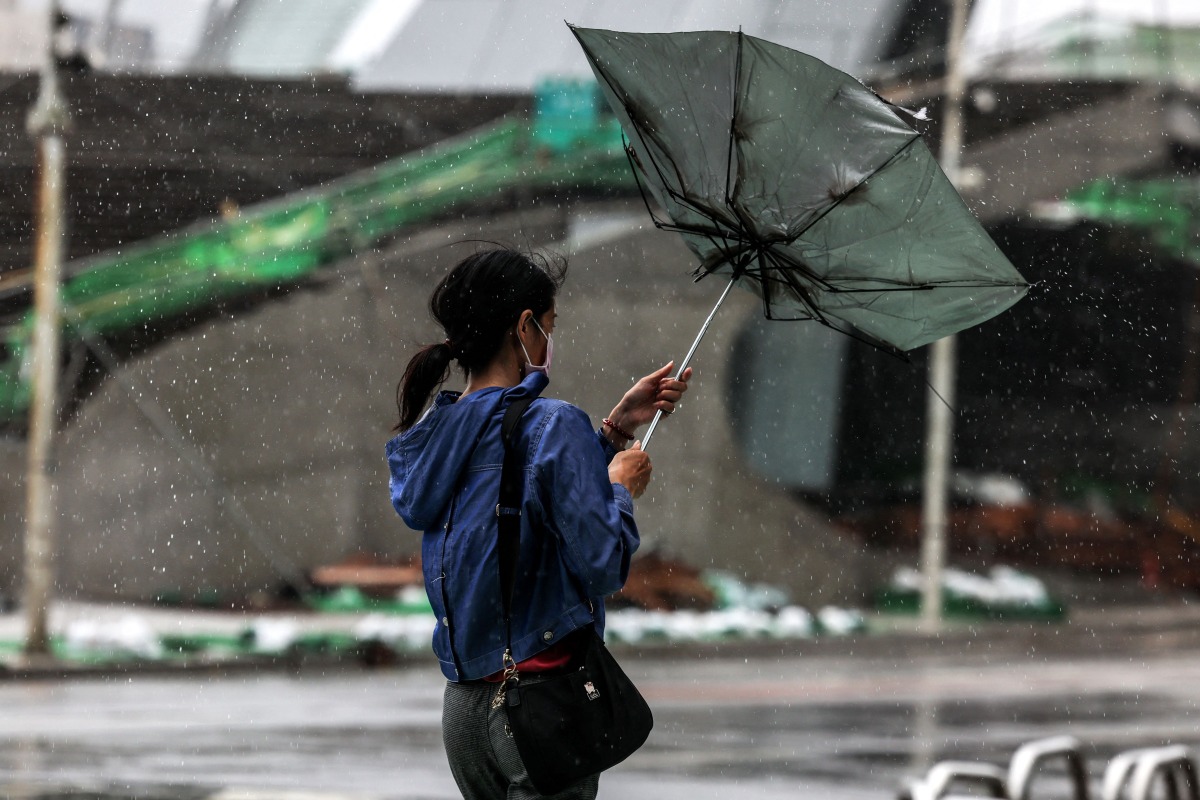 A woman struggles with an umbrella in strong winds and rain as typhoon Bavi passes off northeastern Taiwan in Keelung on July 11, 2026. More than 14,000 people in Taiwan have fled their homes, and many shops remain closed, as a typhoon pounding Japan's remote southwestern islands swept towards China on July 11. (Photo by I-Hwa Cheng / AFP)