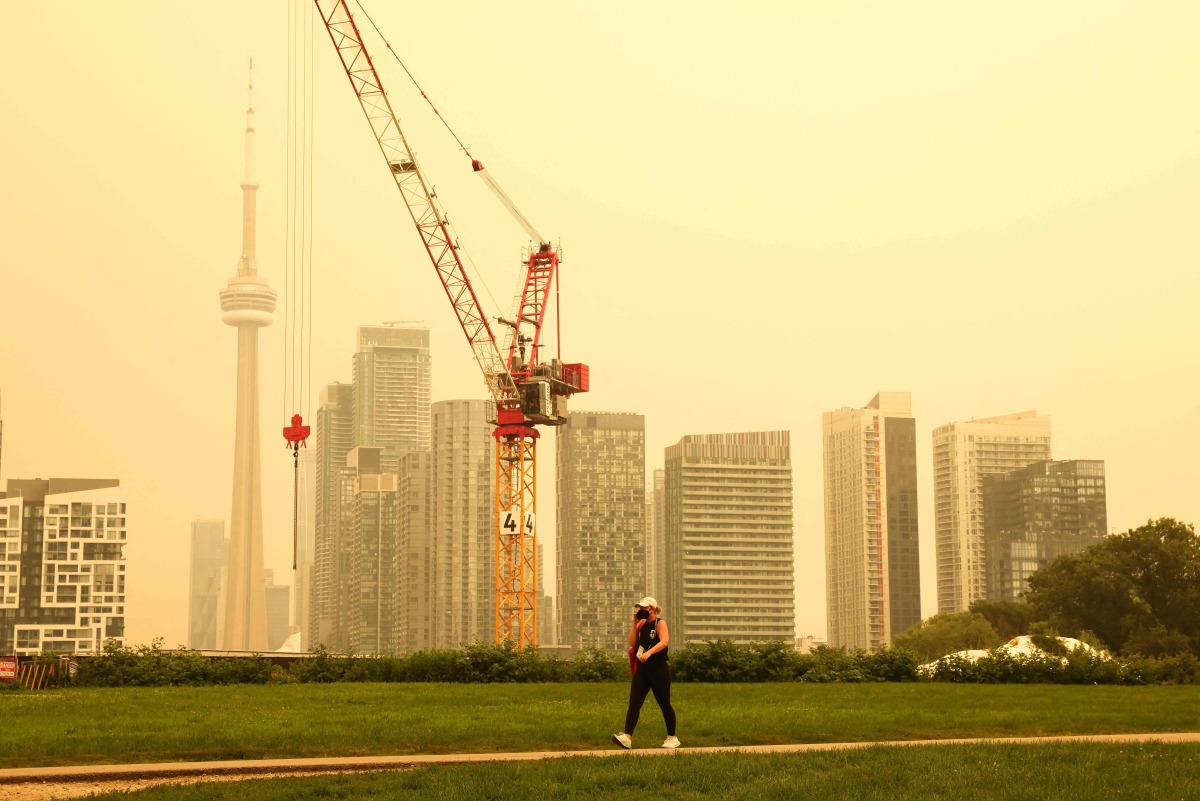 A person walks by the skyline of downtown Toronto, as smoke from forest fires in Northern Ontario causes poor air quality over the city, in Toronto, Ontario, Canada, Wednesday, July 15, 2026. (Photo by Cole BURSTON / AFP)