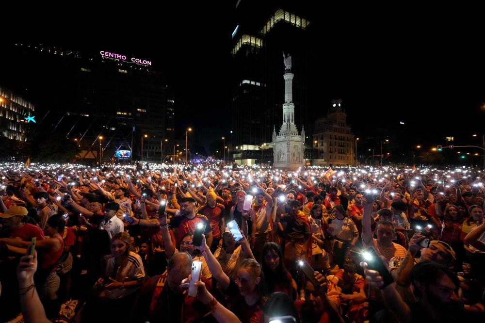 Spain's supporters turn on their phone flashlight as they watch the 2026 World Cup final match between Spain and Argentina displayed on giant screens underneath the Christopher Columbus statue on Colon square's in Madrid, on July 19, 2026. (Photo by Paul Hanna / AFP)