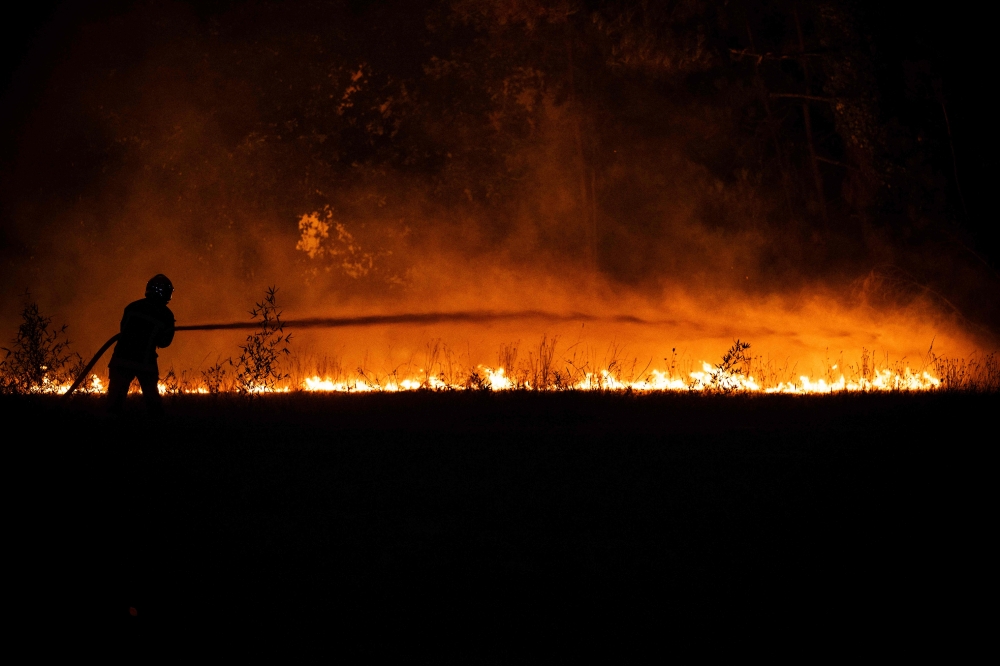 A firefighter sprays water on a burning forest close to a residential area during a wildfire near Lege-Cap-Ferret, southwestern France, on July 23, 2026. (Photo by Julien De Rosa / AFP)