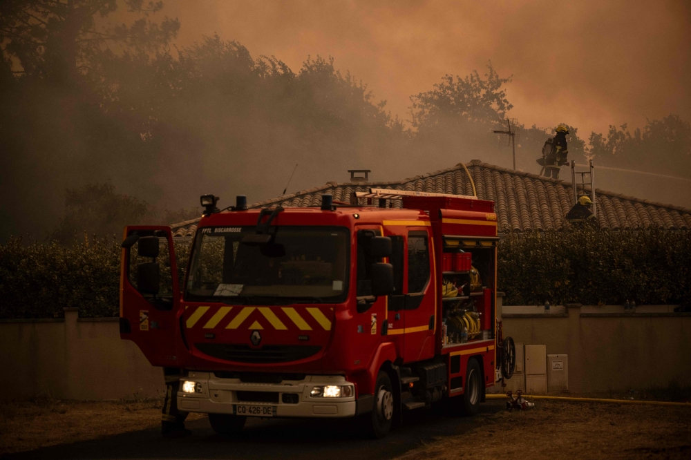 Firefighters spray water with a hose from the roof of a house during a wildfire near Lege Cap Ferret, southwestern France on July 23, 2026. (Photo by Julien De Rosa / AFP)
 