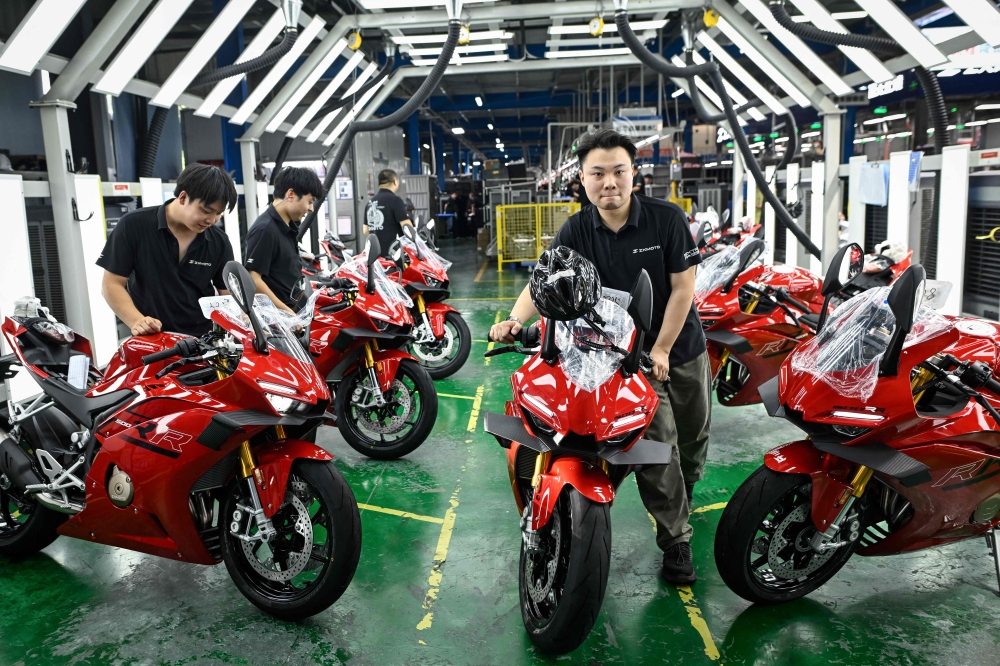This picture taken on July 20, 2026 shows workers preparing to test assembled motorcycles at the ZXMOTO factory in Chongqing, southwestern China. (Photo by Wang Zhao / AFP) 