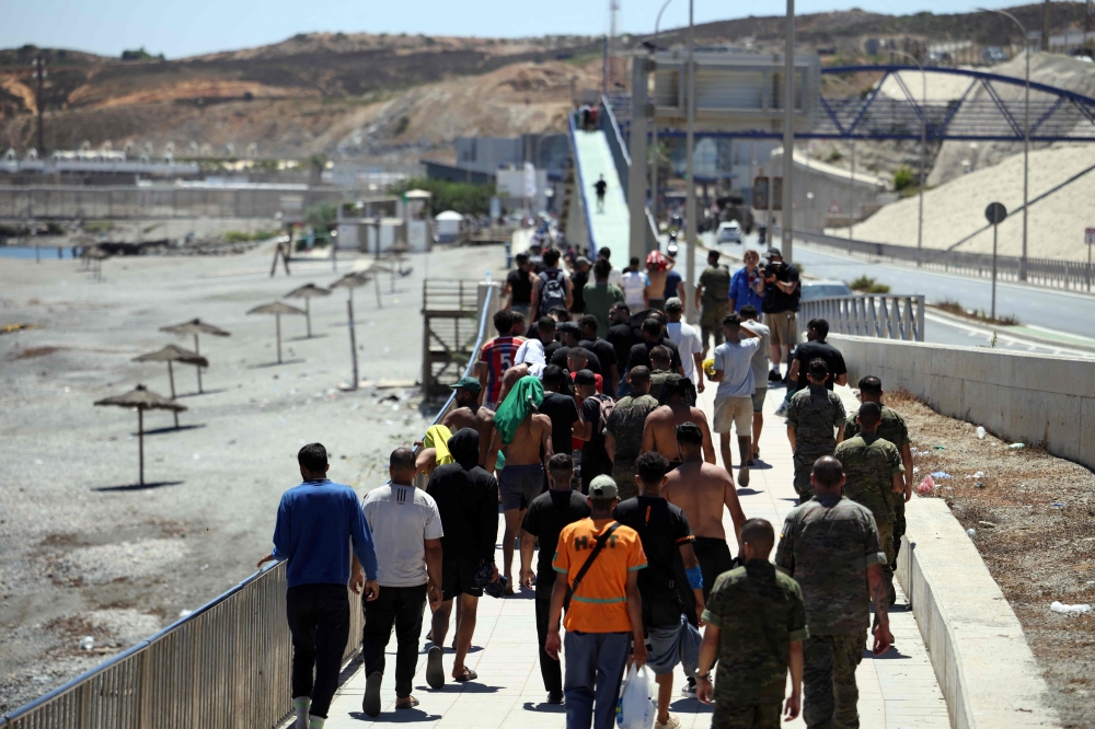 A group of migrants approach the border post to make their way back to Morocco, escorted by Spanish infantry soldiers, in the Spain's north African enclave of Ceuta, on August 2, 2026. (Photo by Henry Nicholls / AFP)