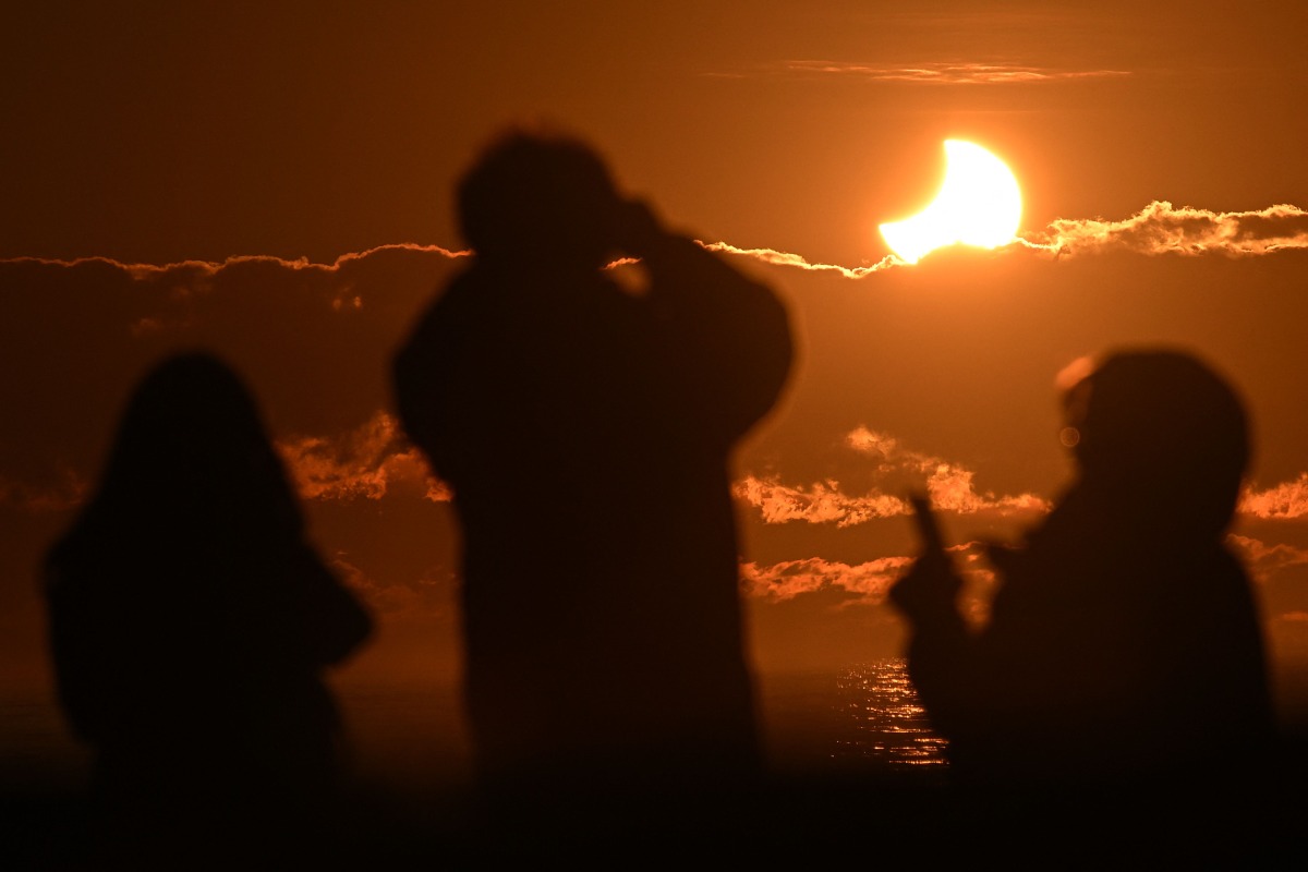 People watch a partial solar eclipse at New Brighton, a coastal suburb of Christchurch, on September 22, 2025. Photo by Sanka Vidanagama / AFP