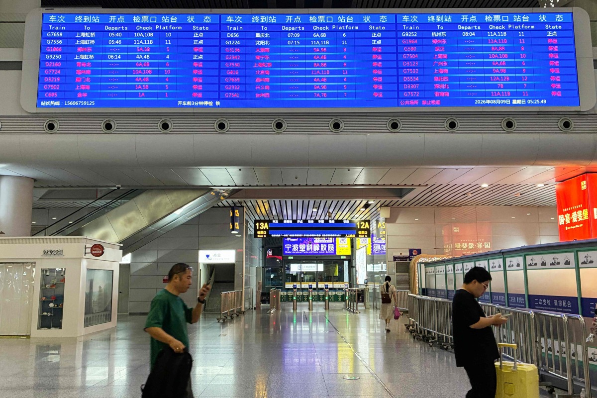 Passengers walk under a departure board at Ningbo railway station as most trains are cancelled due to approaching Typhoon Dolphin on August 9, 2026. (Photo by Rebecca BAILEY / AFP)