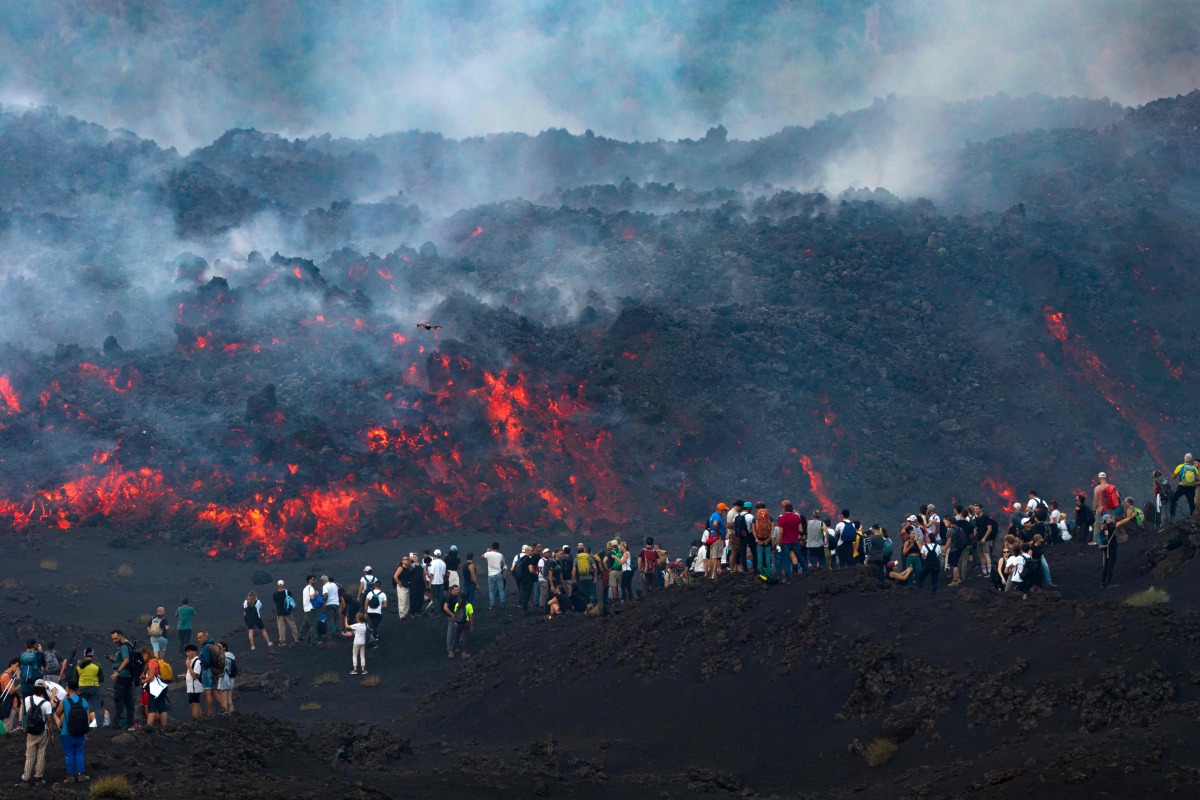 This handout photograph taken by Etna Walk on August 11, 2026 and obtained on August 12, 2026 shows visitors standing next to lava flowing from Mount Etna volcano during an eruption, in Catania, in the Mediterranean island of Sicily. (Photo by Handout / Etna Walk / AFP)