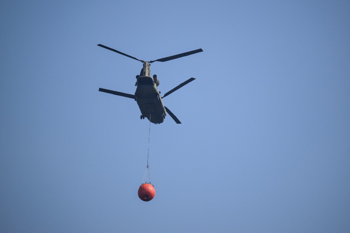 A Royal Netherlands Air Force Boeing CH-47D Chinook carrying a bambi bucket departs from Baelen, near Eupen, eastern Belgium to tackle a wildfire burning in the Hautes Fagnes (High Fens) nature reserve on August 16, 2026. Photo by JOHN THYS / AFP