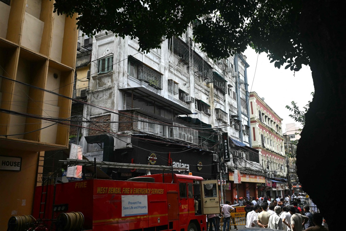 Onlookers and fire personnel gather at the site following a fire at a hotel in Kolkata on August 19, 2026. Photo by Dibyangshu SARKAR / AFP