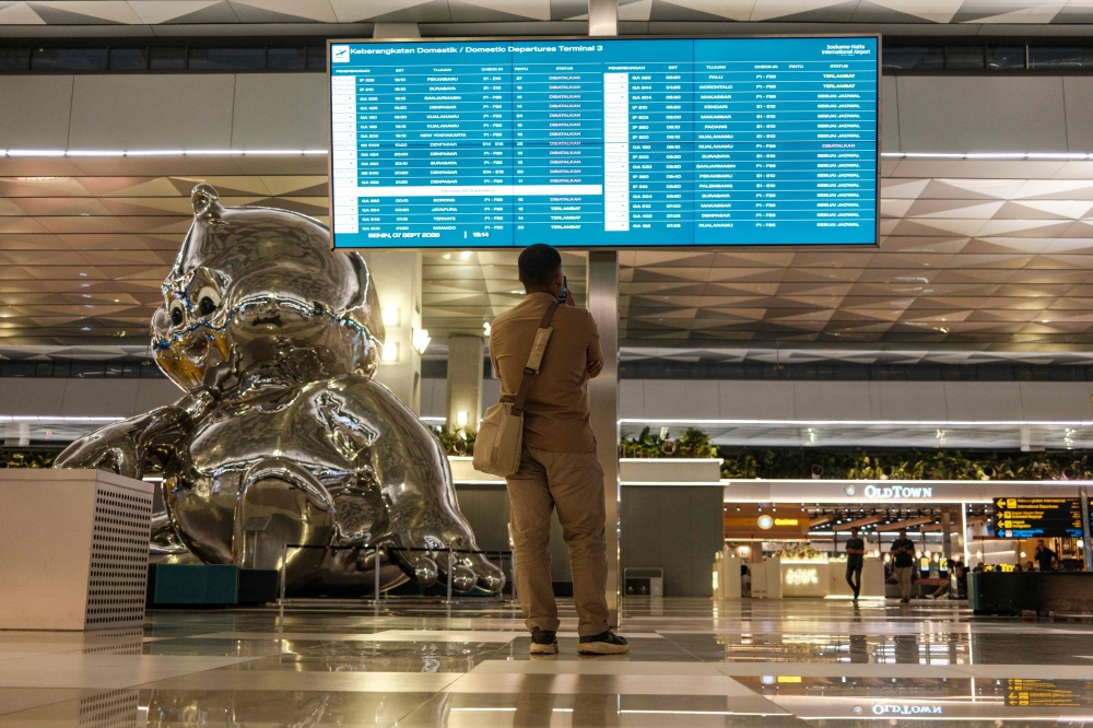 A stranded passenger looks at a flight information screen amid the closure of Soekarno-Hatta International Airport due to the eruption of the Mount Anak Krakatau volcano, in Tangerang on September 7, 2026. indonesia's main airport and several other air travel hubs reopened early on September 8 after days of closure due to ash from a volcanic eruption, the Transport Ministry said. (Photo by Taris HIRZIMAN / AFP)