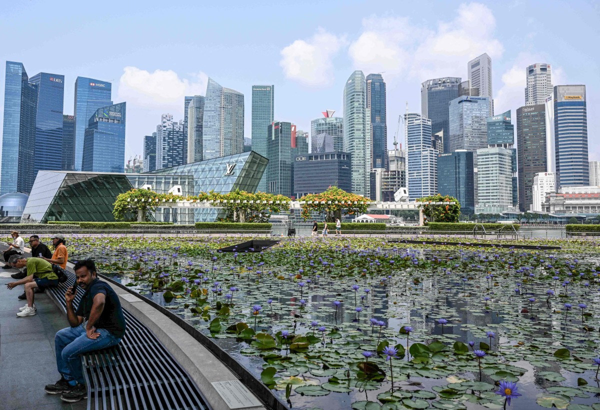 People sit next to a pond outside ArtScience museum at Marina bay in Singapore on September 8, 2026. (Photo by Roslan RAHMAN / AFP)