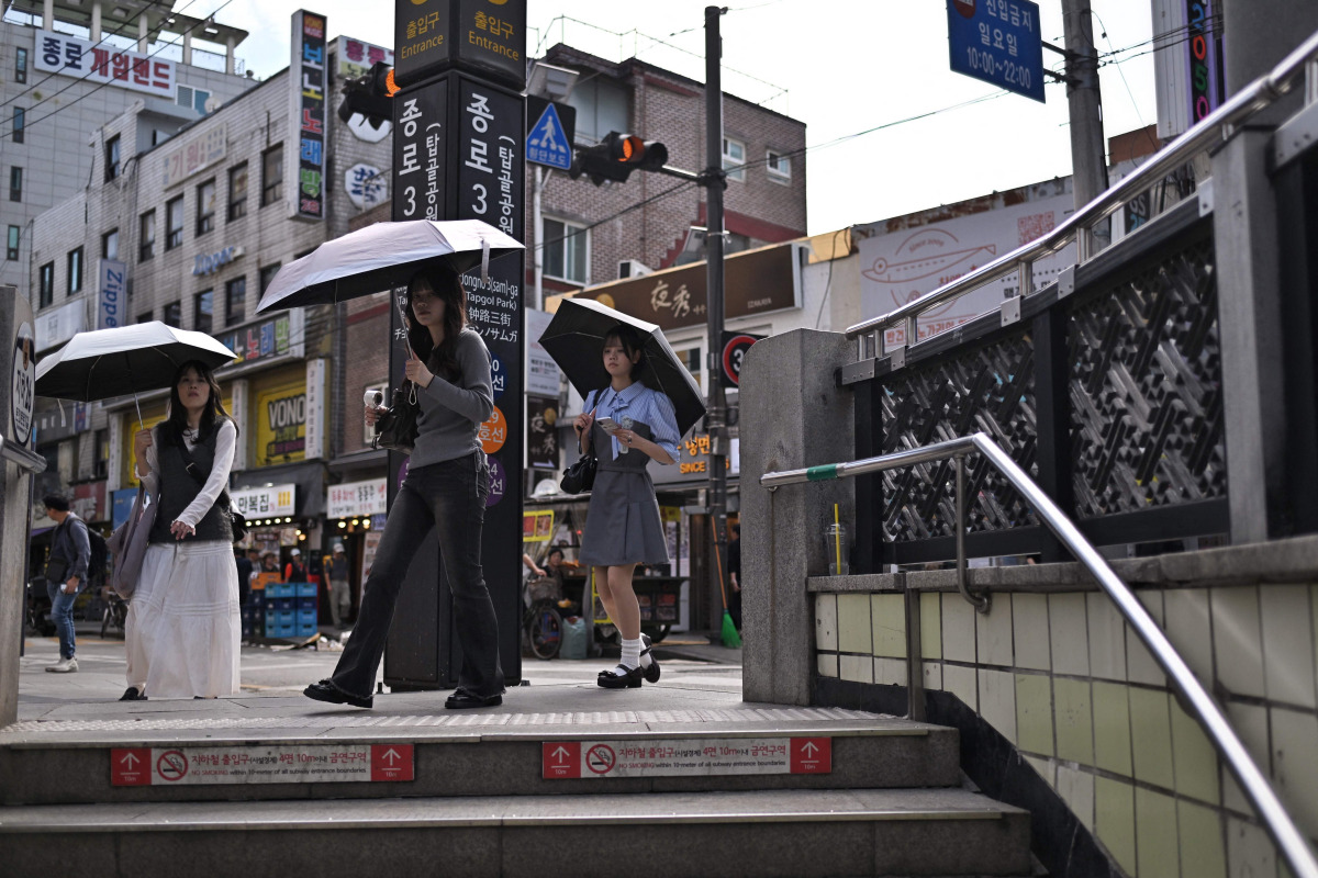 People shield themselves with umbrellas while walking past the metro station entrance in Jongno 3-ga in Seoul on September 20, 2026. (Photo by Lillian SUWANRUMPHA / AFP)