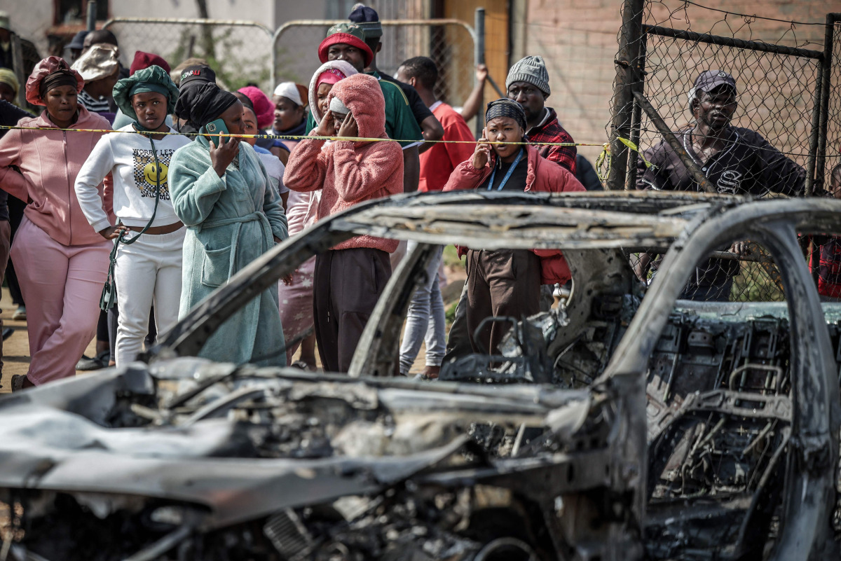 Residents stand behind police tape near the scene where gunmen armed with assault rifles stormed a bar in Johannesburg on September 27, 2026. Photo by EMMANUEL CROSET / AFP