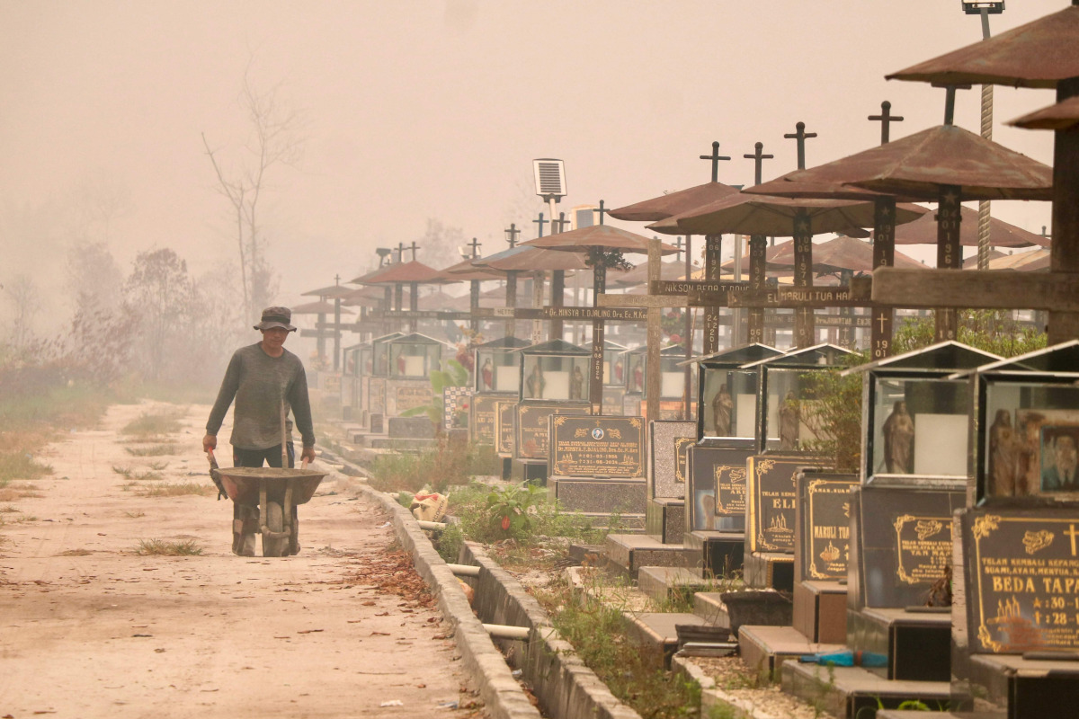 A worker pushes a wheelbarrow through a public cemetery blanketed in thick smoke haze caused by forest and land fires in Palangka Raya, Central Kalimantan province on September 30, 2026. (Photo by REINA / AFP)
