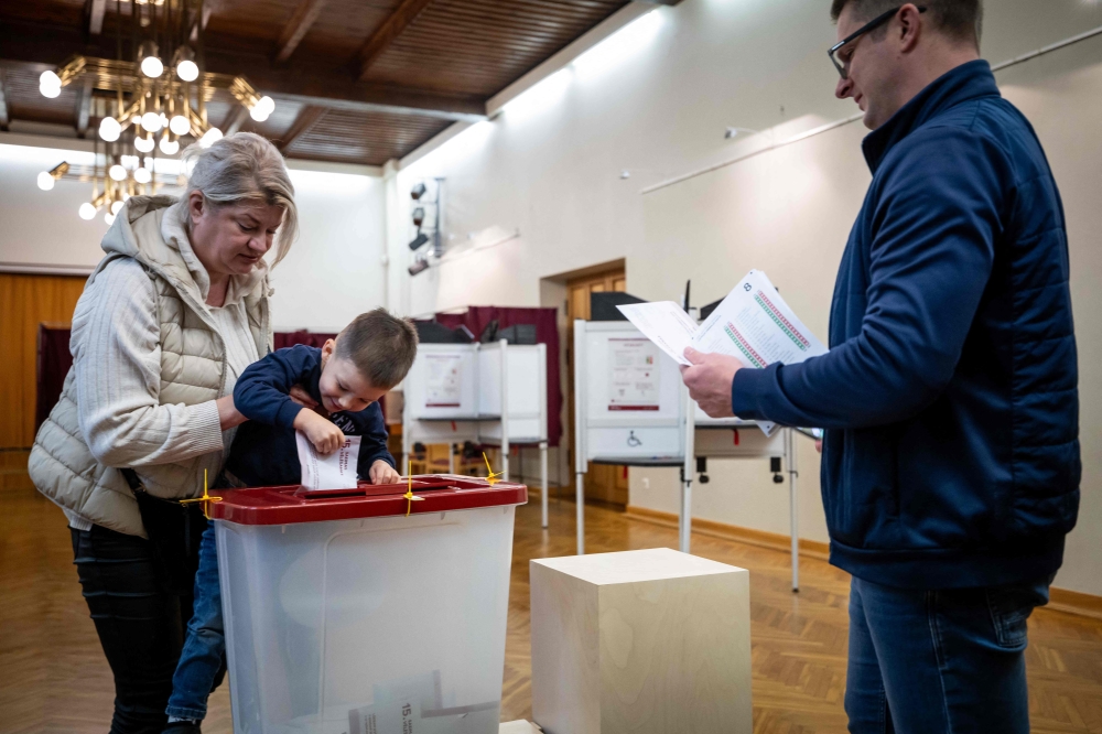 A child accompanied by his parents casts a ballot at a polling station during Latvia's parliamentary elections in Riga on October 3, 2026. (Photo by Wojtek Radwanski / AFP)