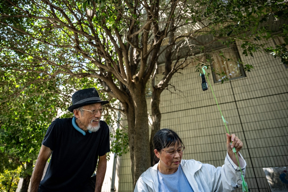 In this picture taken on August 25, 2026, activists Kaoru Morimoto (L) and Susumu Nirasawa check the temperature under a tree in the Nakano district of Tokyo. (Photo by Philip Fong / AFP)