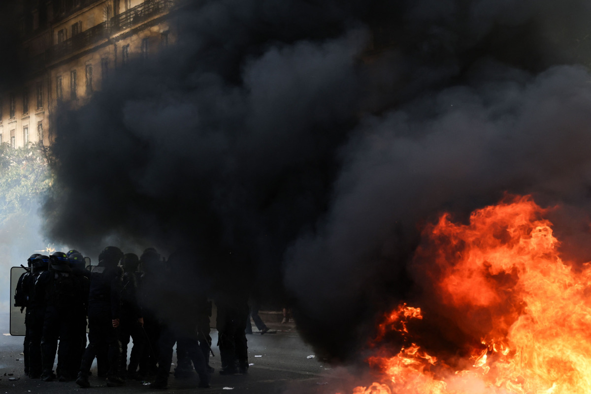 Police officers stand guard by bins and furniture set on fire in the street during a demonstration of high-school students, in Paris on October 6, 2026, as part of a nationwide protest movement over learning conditions. (Photo by Kenzo TRIBOUILLARD / AFP)

