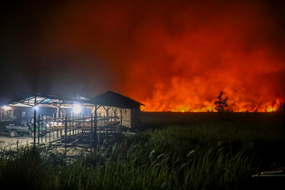 Flames and thick smoke glow against the night sky as a massive wildfire burns near residential structures in the Panarung area of Palangkaraya, Central Kalimantan province, on October 8, 2026. (Photo by REINA / AFP)
