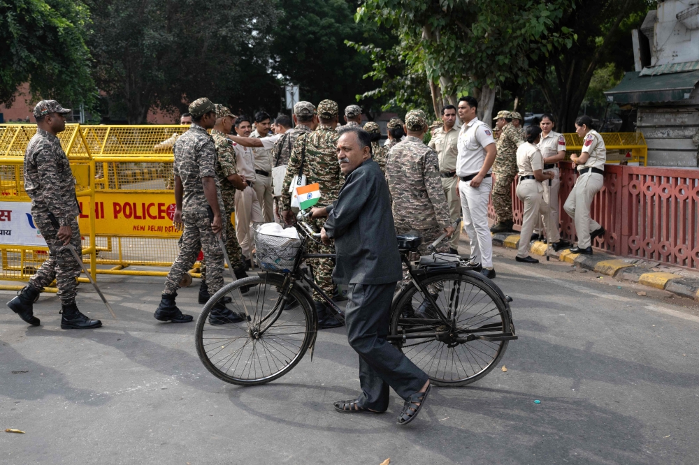 A man pushing his cycle walks past a temporary checkpoint amid ongoing protests, near Jantar Mantar in New Delhi on October 11, 2026. (Photo by Sajjad Hussain / AFP)