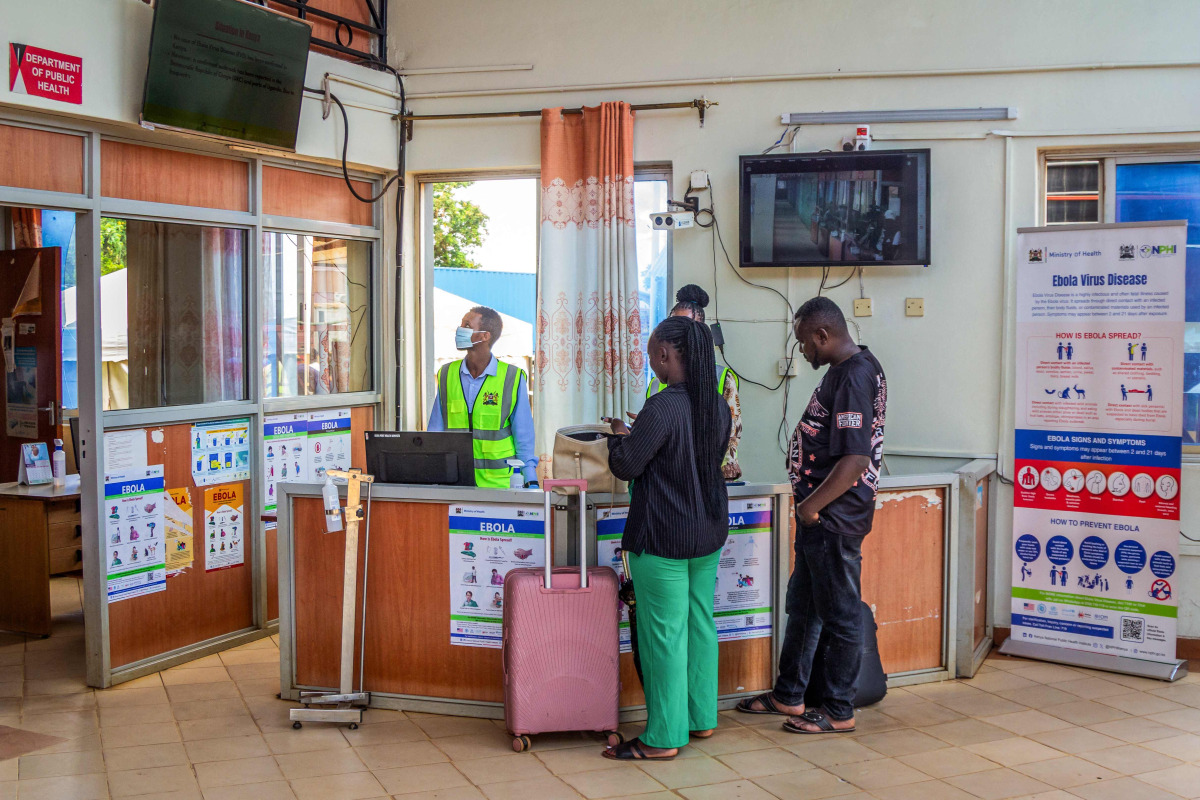 Travellers receive information from health officials near Ebola awareness posters before crossing the border at the Busia One Stop Border Post (OSBP) on the Kenya-Uganda border as health authorities step up Ebola screening measures, in Busia on October 12, 2026. (Photo by Bright Emoja / AFP)
