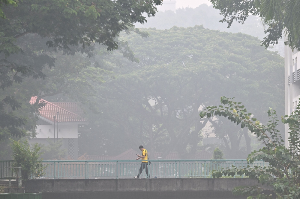 This picture provided by The Straits Times taken and received on October 14, 2026 shows a man walking on a road as the city is shrouded with haze in Singapore. (Photo by The Straits Times / AFP)