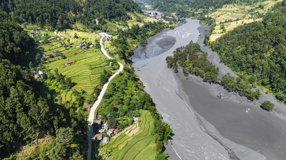 An aerial view shows muddy water flowing through the Budhi Gandaki river, separating Nepal's Gorkha (L) and Dhading districts on October 14, 2026, in the aftermath of a flash flood caused by a dry landslide. (Photo by Prakash Mathema / AFP)