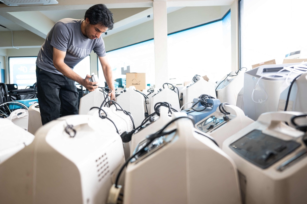 A technician inspects oxygen concentrators awaiting repair and cleaning at a medical supply warehouse in Kuala Lumpur on October 15, 2026. (Photo by Mohd Rasfan / AFP) 
