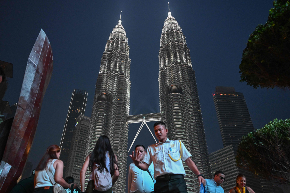 People walk past the Petronas Tower in Kuala Lumpur on October 18, 2026. (Photo by Jam STA ROSA / AFP)