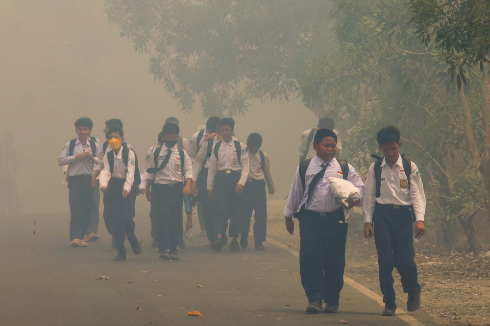 Schoolchildren walk along a smoke-shrouded road in Tegal Arum, Banjarbaru, South Kalimantan, on October 20, 2026, as massive forest and land fires blanket the area in thick haze. (Photo by Muda Sagala / AFP)