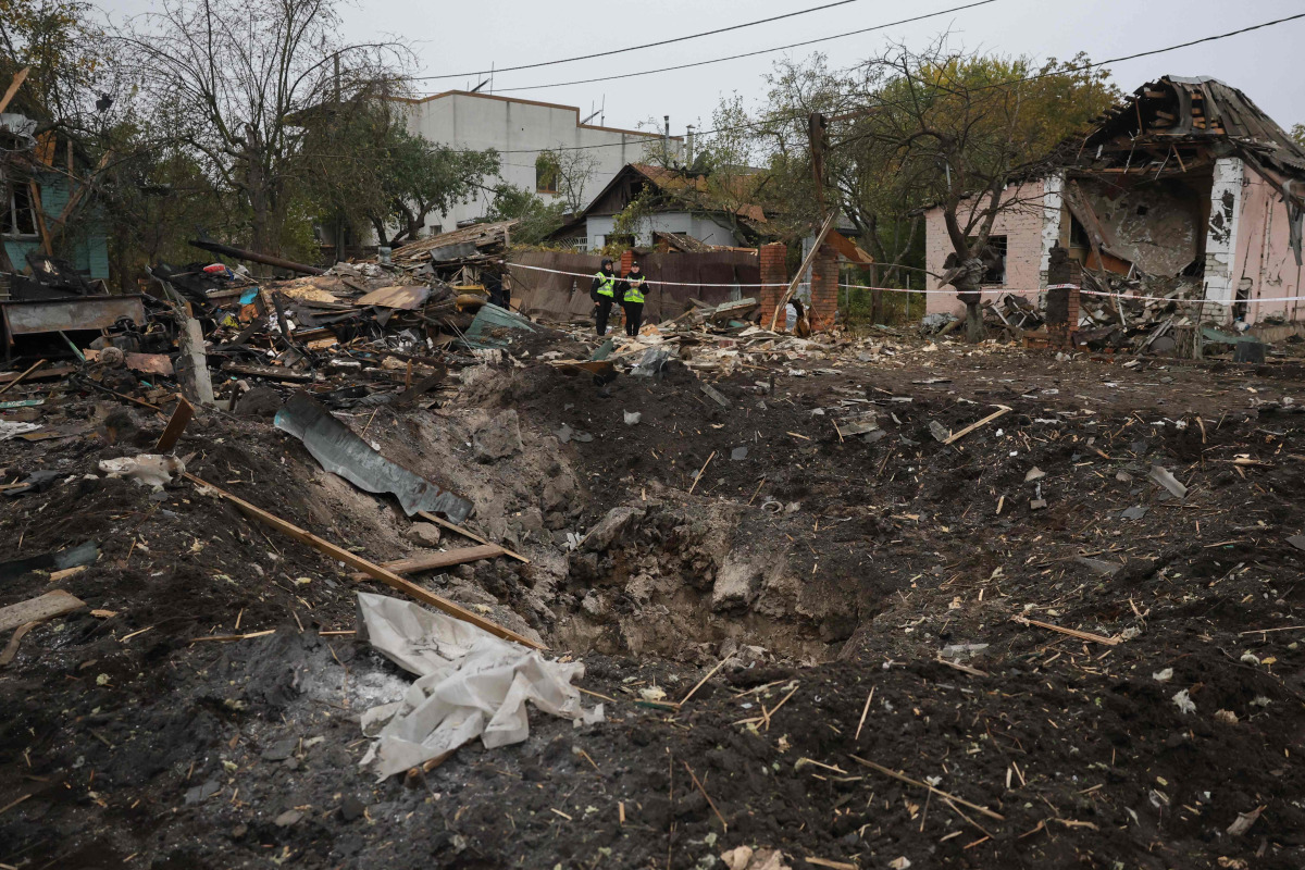Ukrainian police officers stand next to a crater at the site of a missile strike in Kyiv on October 22, 2026. (Photo by Serhii DILIN / AFP)