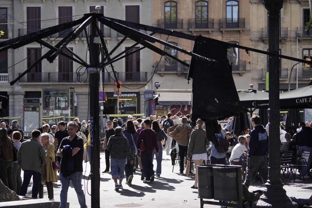 People walk past a burnt sunshade on a terrace damaged during overnight riots in Catalunya square in Barcelona, on October 25, 2026. (Photo by Manaure Quintero / AFP)
 