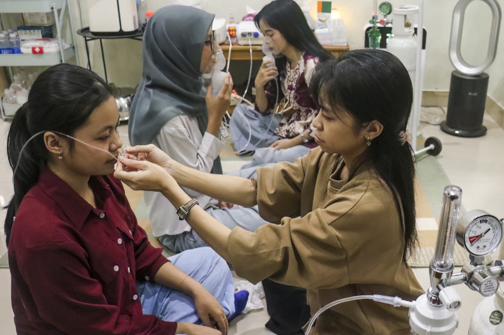 A volunteer (R) assists a woman with a nasal oxygen cannula at a shelter to aid residents experiencing respiratory difficulties in Palangkaraya, Central Kalimantan province on October 26, 2026. Photo by REINA / AFP